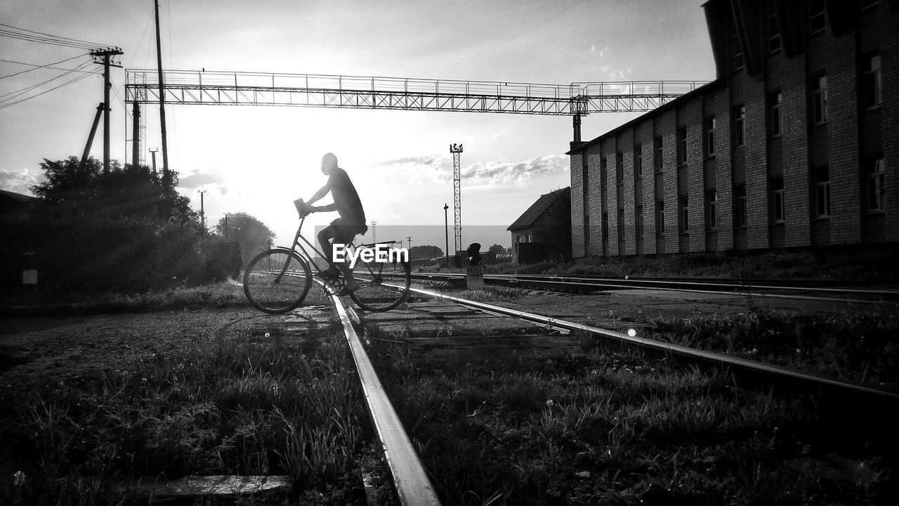 Man riding bicycle on railroad track against sky
