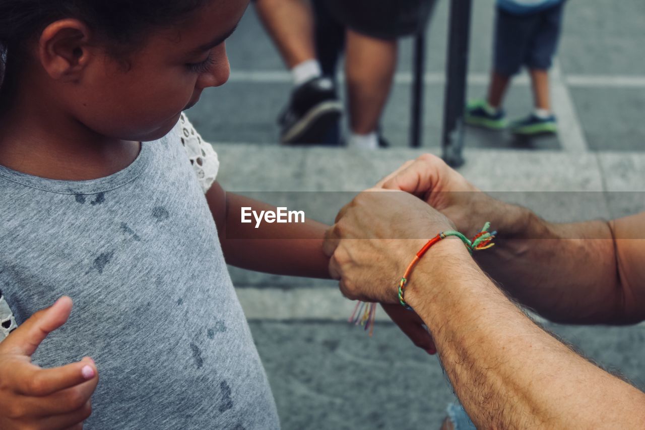 Cropped hands of man tying string on girl arm