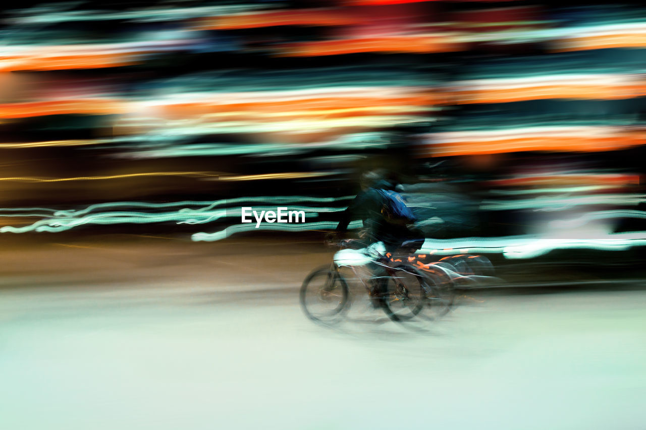 Blurred image of persona riding bicycle against light trail at night