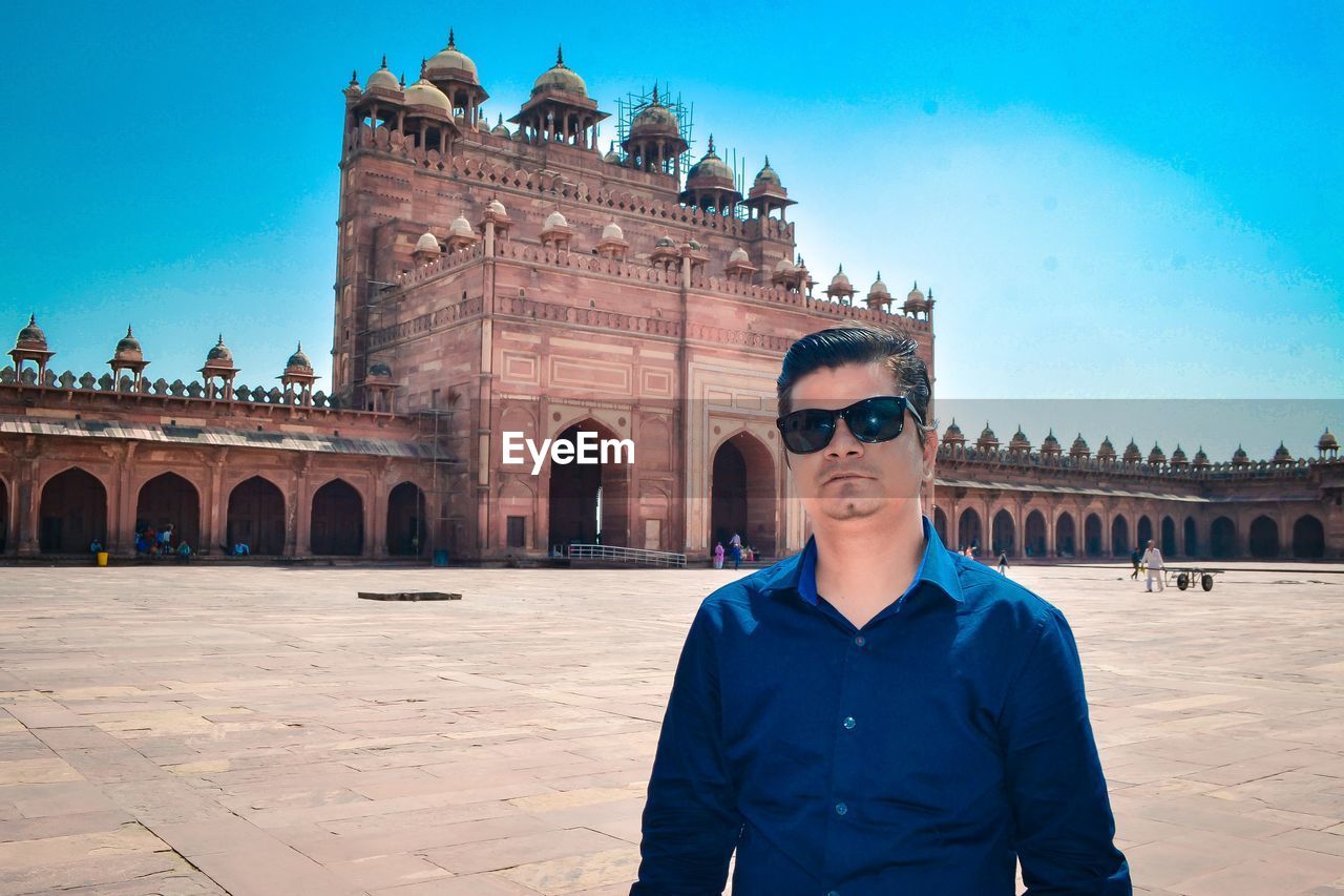 Portrait of man wearing sunglasses standing against fort