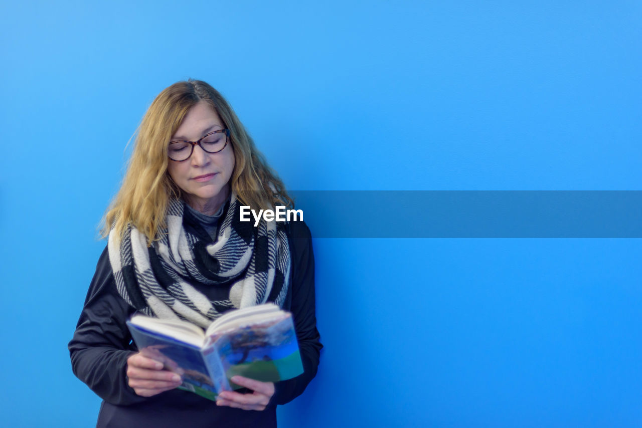 Woman reading book against blue background