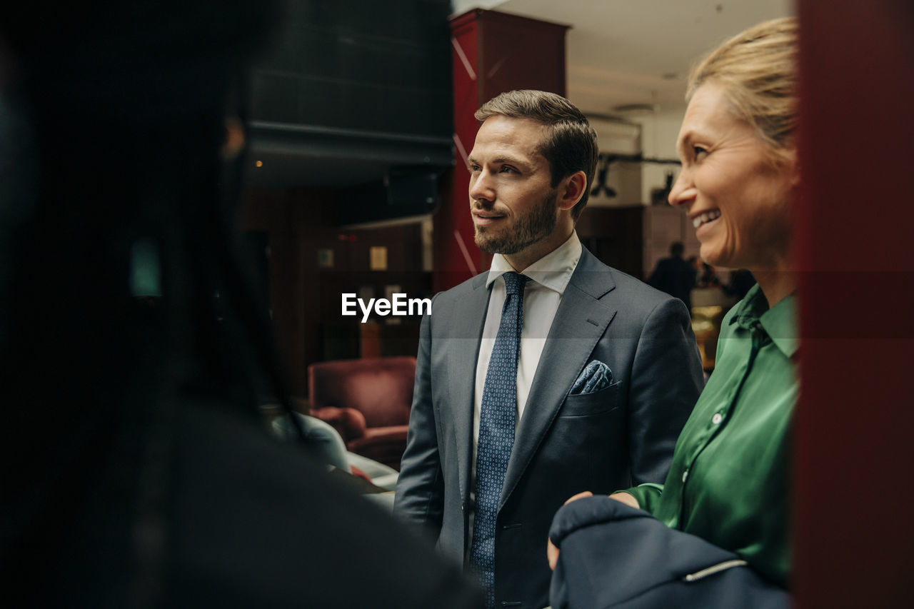 Smiling mature businesswoman standing by male professional in hotel lounge