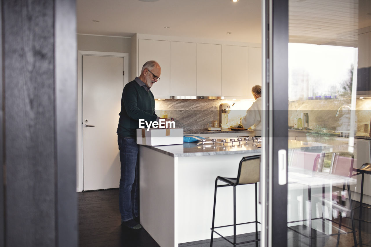 Full length of senior man unpacking box over kitchen island