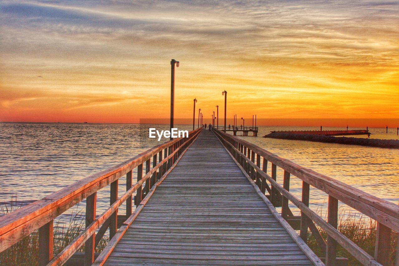 Pier over sea against sky during sunset