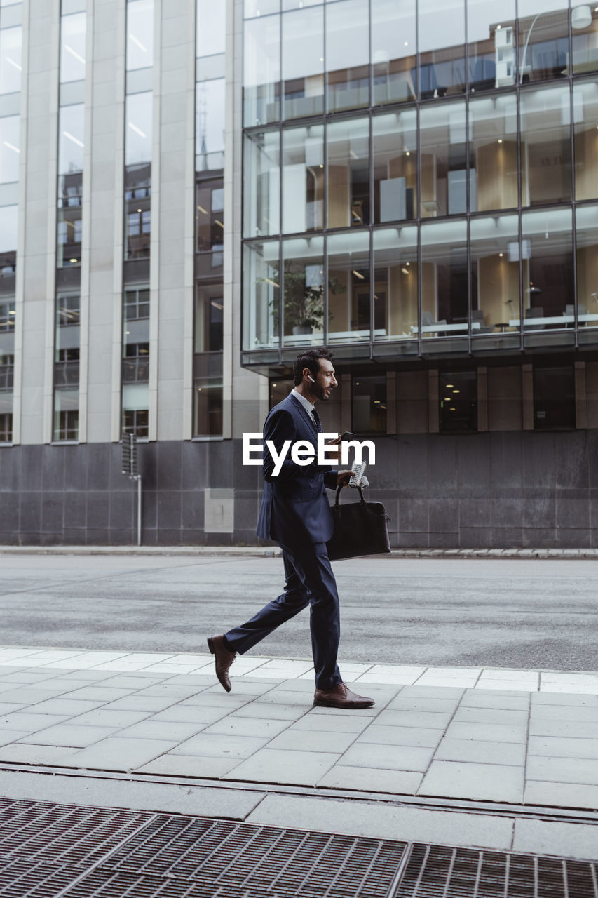 Entrepreneur with bag using smart phone while walking in city