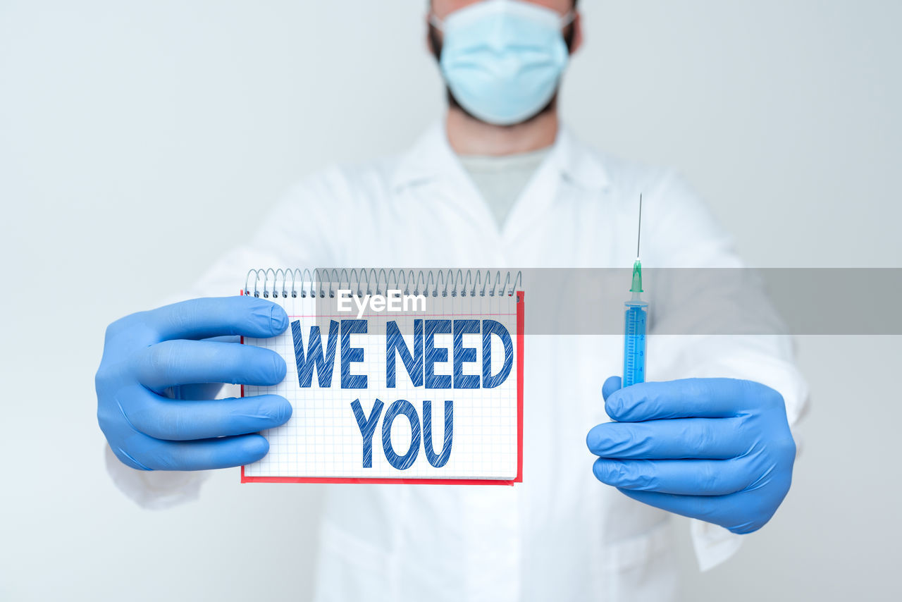 Midsection of doctor wearing mask holding syringe against white background