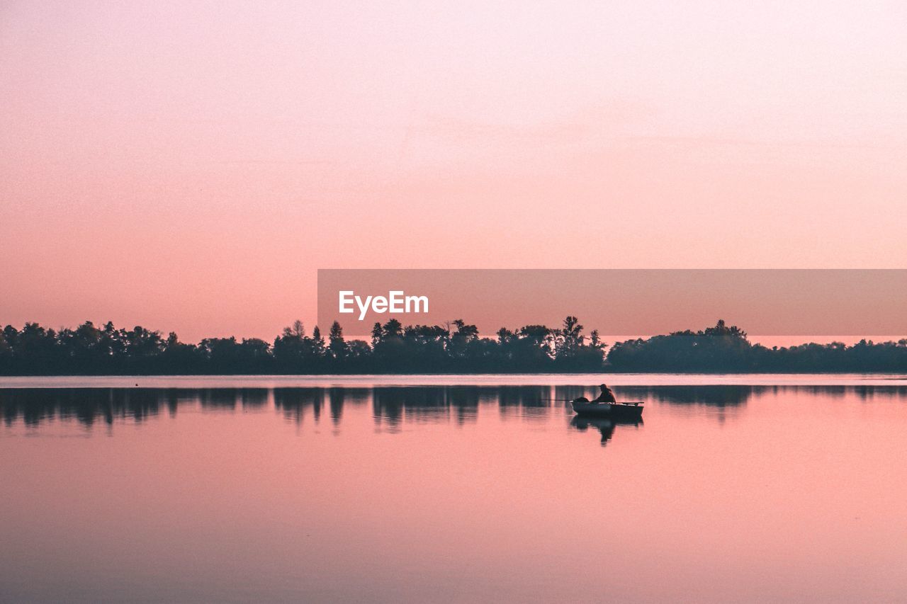 Person in boat on lake against clear sky during sunset