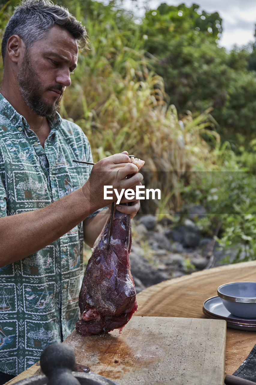 Chef preparing local venison leg for roasting on barbecue