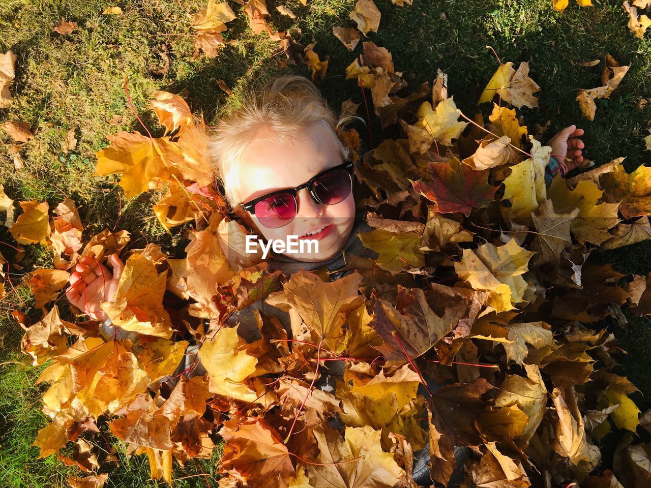 Portrait of girl covered in leaves on field during autumn