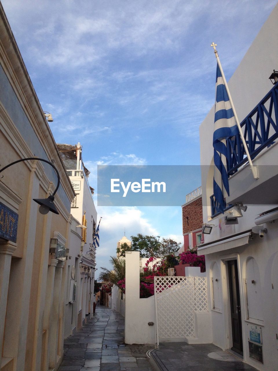 Narrow empty alley along buildings with greek flag in foreground