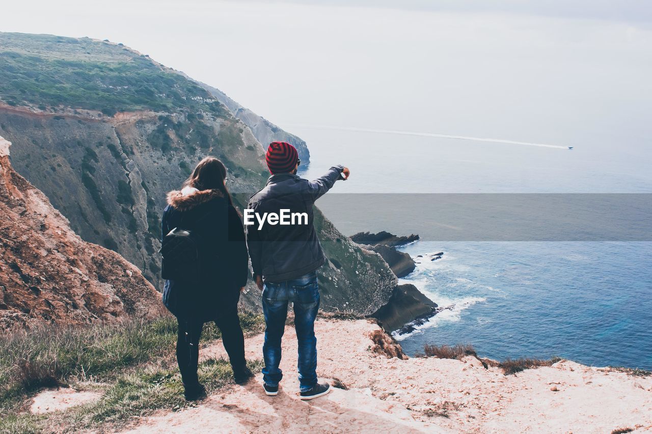 Rear view of couple standing on rock by sea