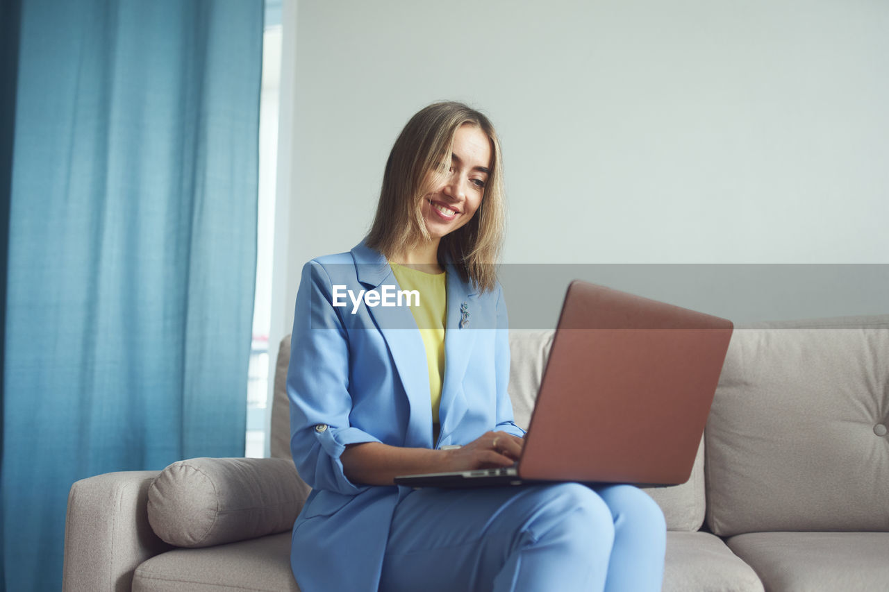 Smiling businesswoman working in laptop sitting on sofa