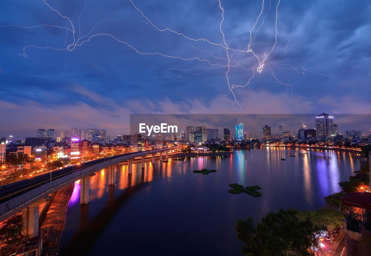 Illuminated city by river against sky at night