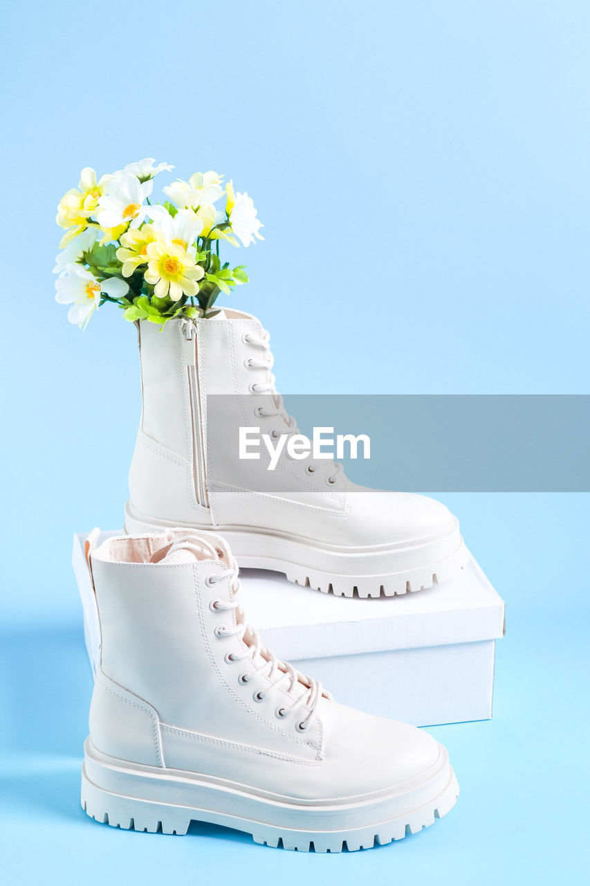 White martens boots with a bouquet of spring flowers and a white cardboard box on a blue.