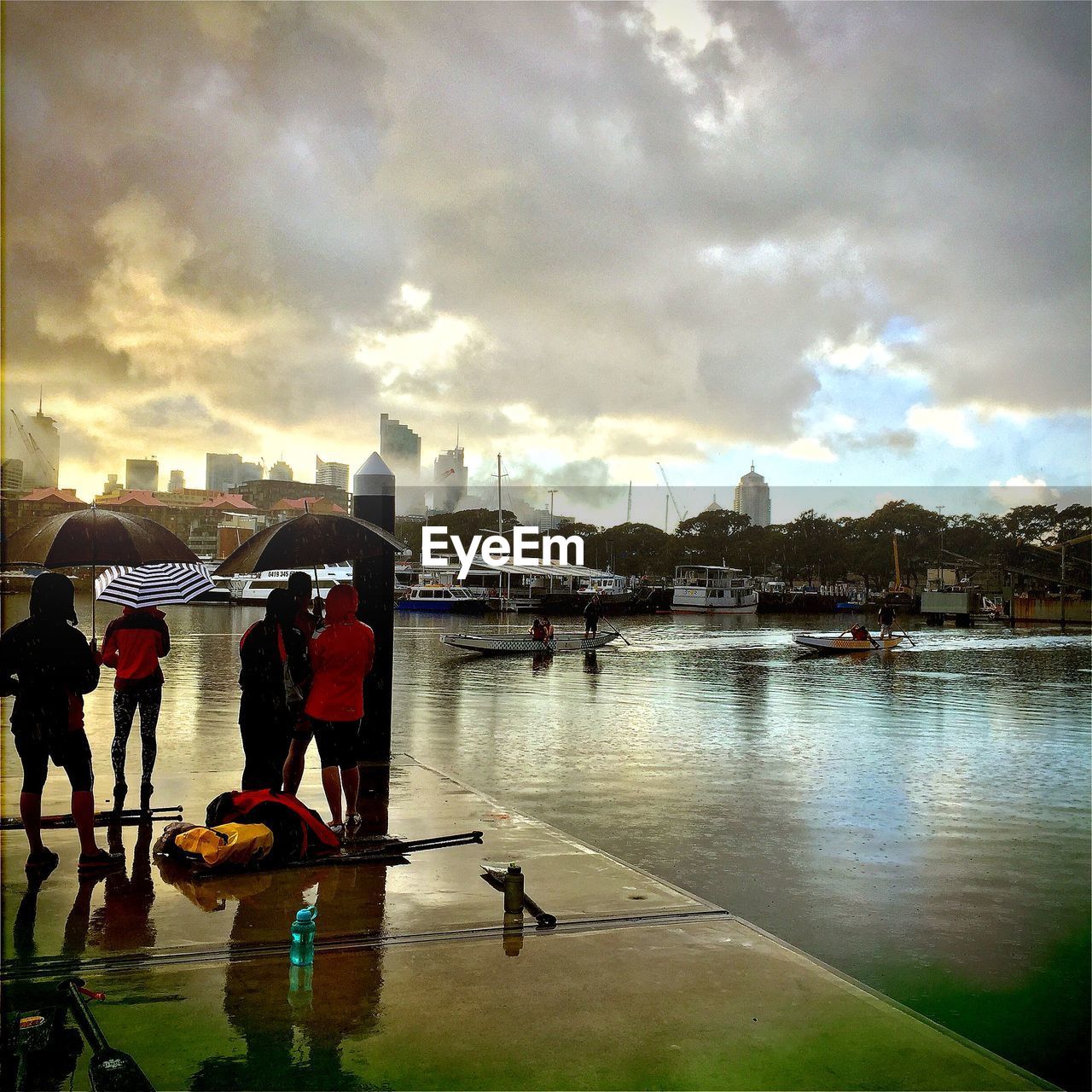 Rear view of people on pier by lake against sky during rainy season