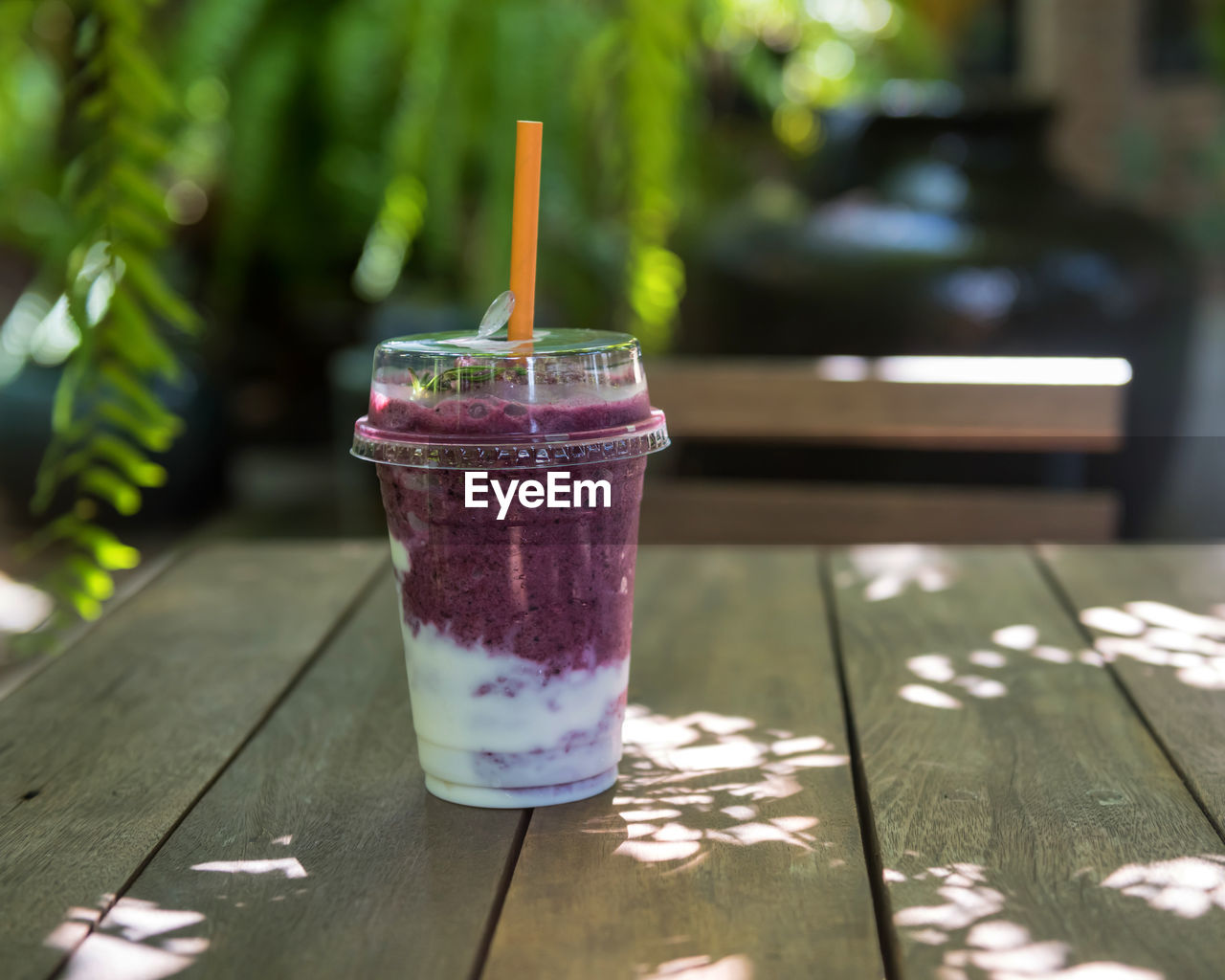 Blueberry yogurt smooties on wooden table of coffee shop garden cafe with blur foliage light