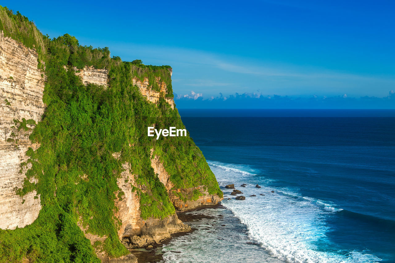 Scenic view of cliff by sea against sky at uluwatu