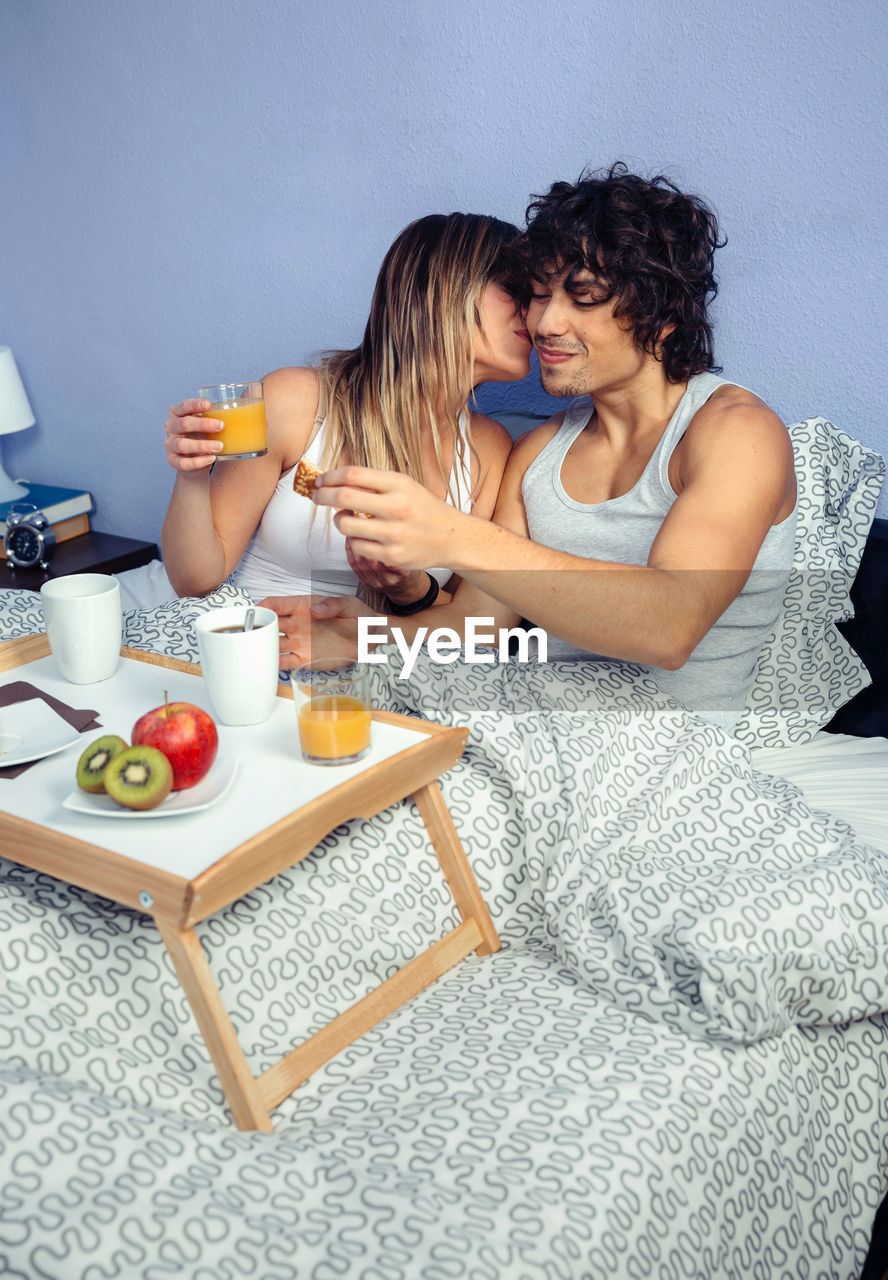 Young couple with food and drinks on bed at home