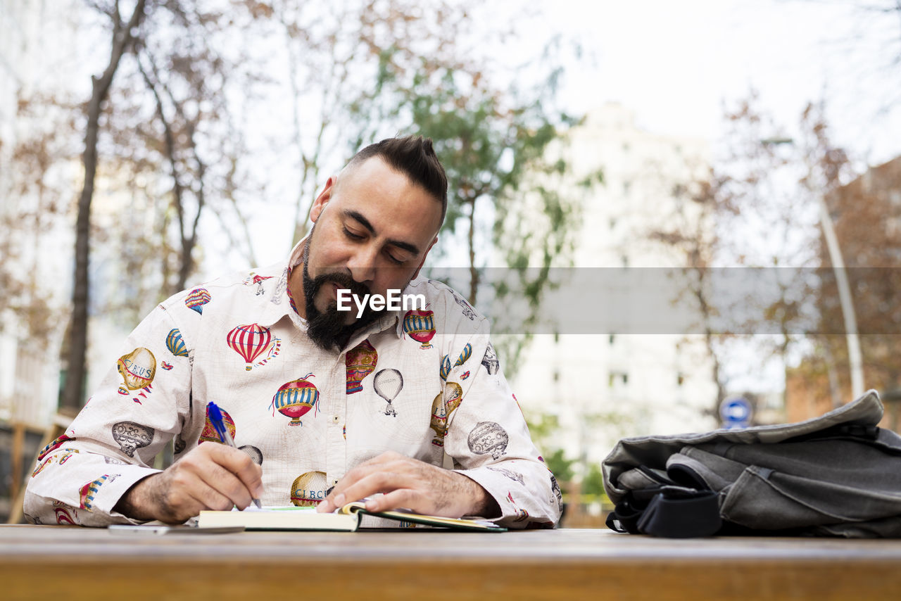 Bearded man sitting outdoors while working over a wooden table