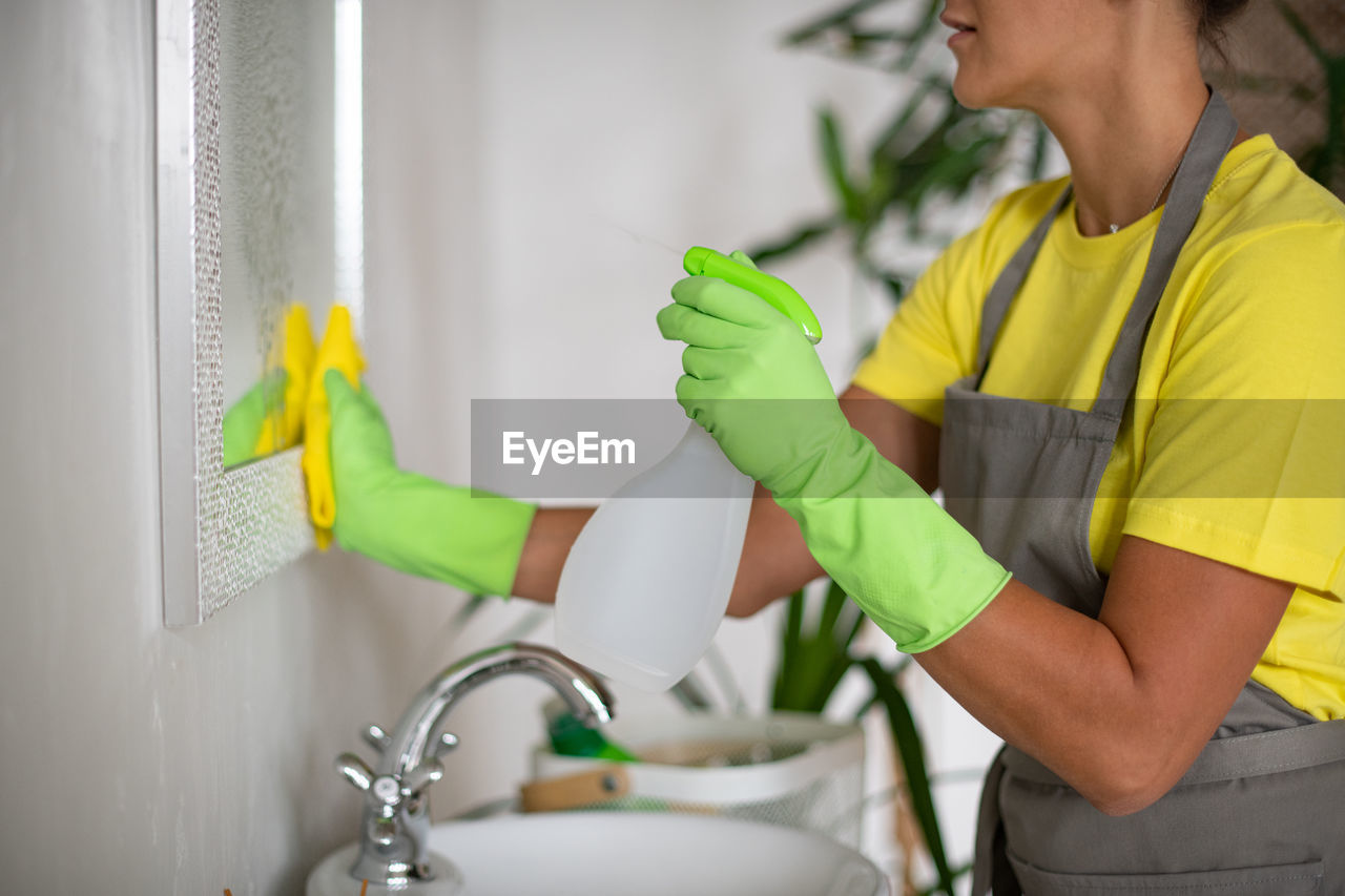 Cleaning the bathroom. the girl rubs the sink and mirror. rubber gloves, apron and cleaning supplies