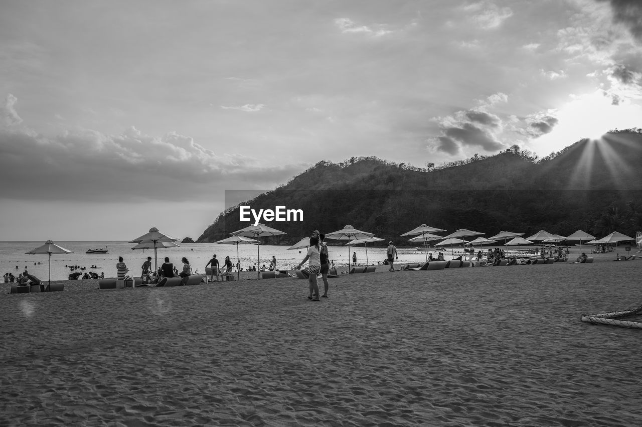 PEOPLE ON BEACH BY MOUNTAINS AGAINST SKY