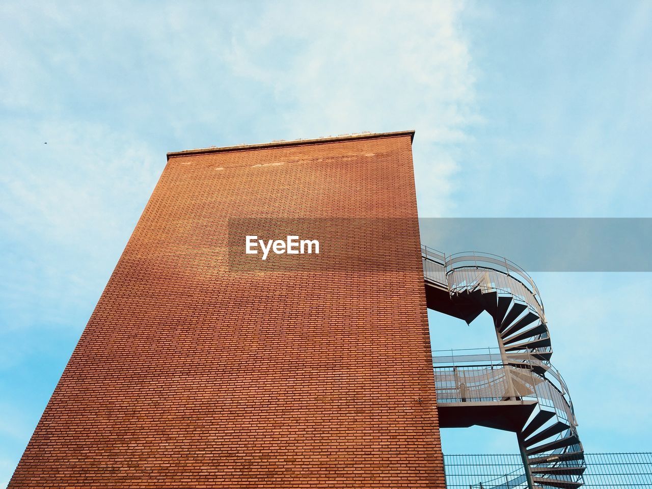 Low angle view of  brick wall building with spiral staircase of fire escape against sky