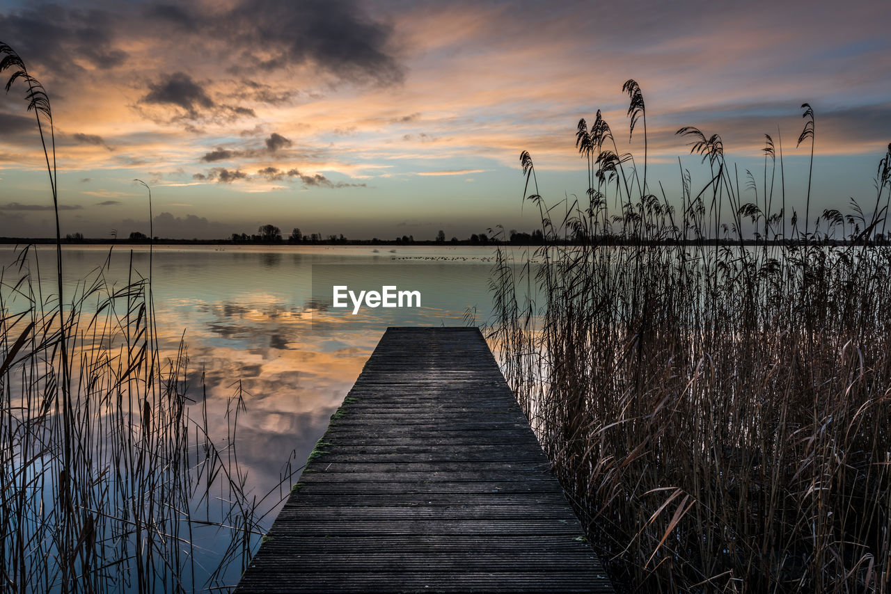 Jetty in lake against sunset sky