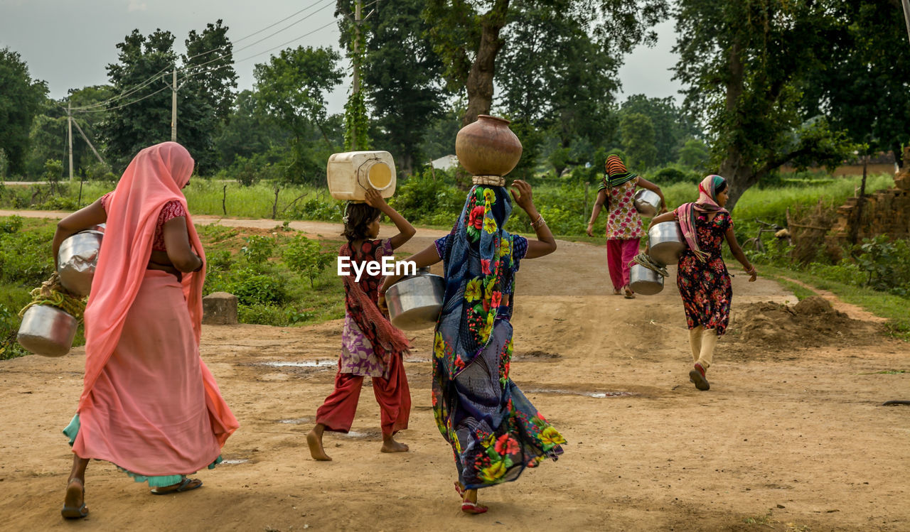 Rear view of woman carrying pitchers while walking on field