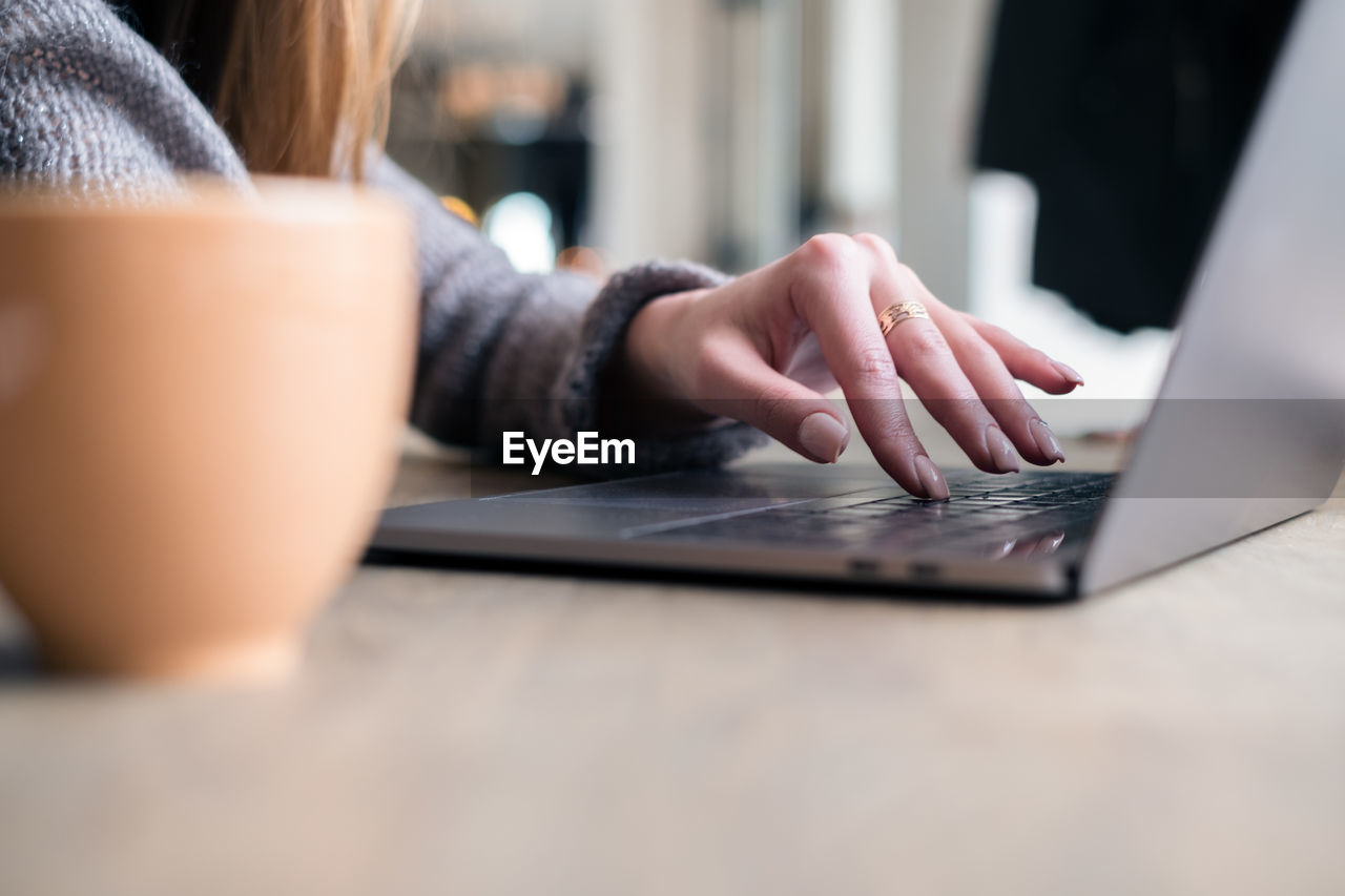 Cropped hand of woman using laptop on table