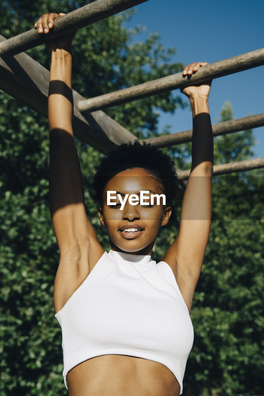 Female athlete looking down while hanging on monkey bar in park