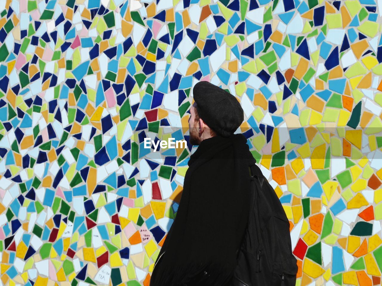 Young man standing against colorful mosaic wall