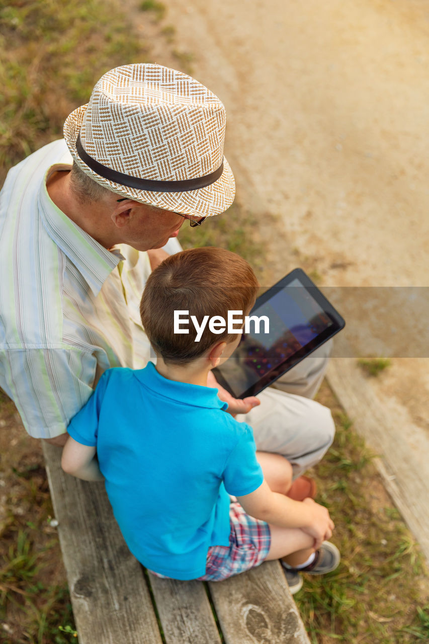 Grandson teaching digital tablet to grandfather while sitting in public park