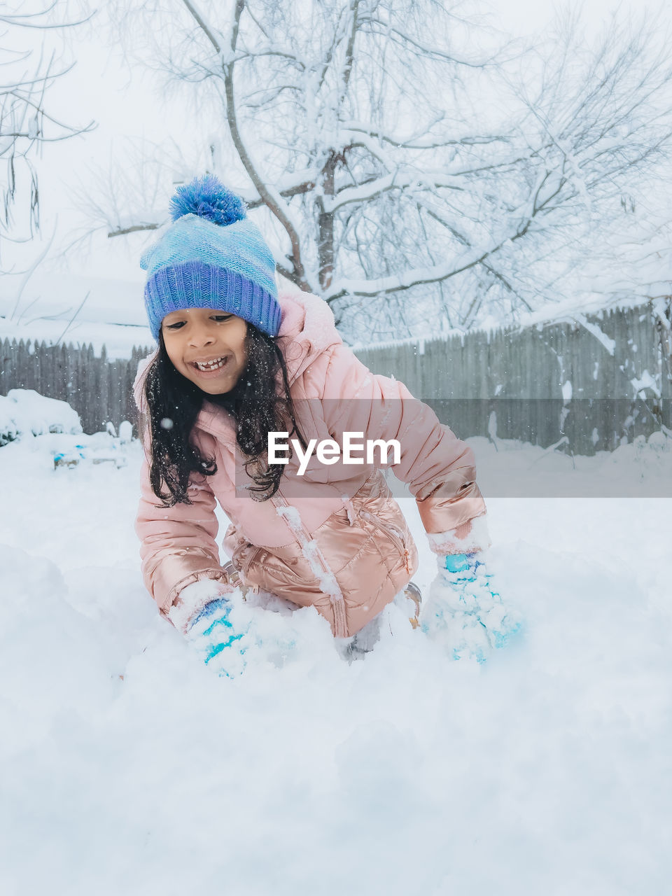Diverse mixed race pre school toddler girl outdoors in winter playing with snow 