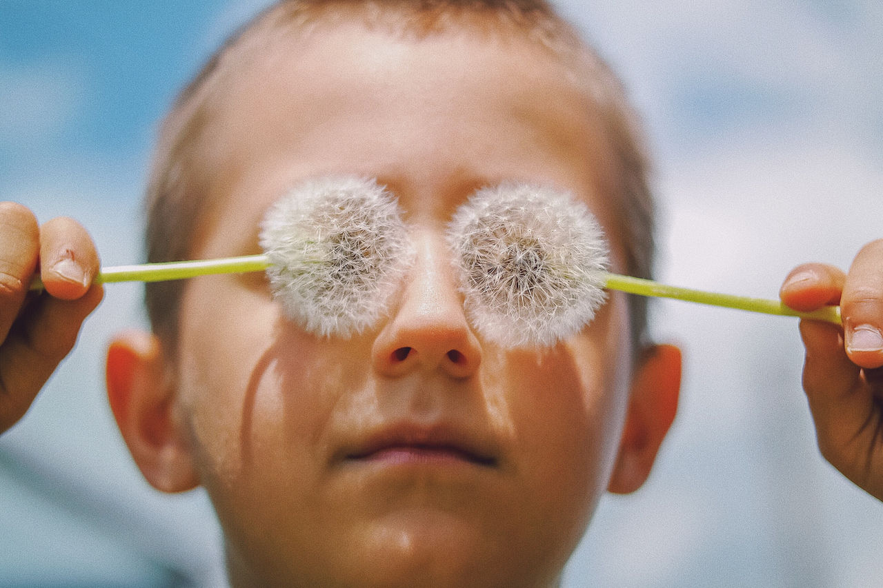 Close-up of boy covering eyes with dandelions