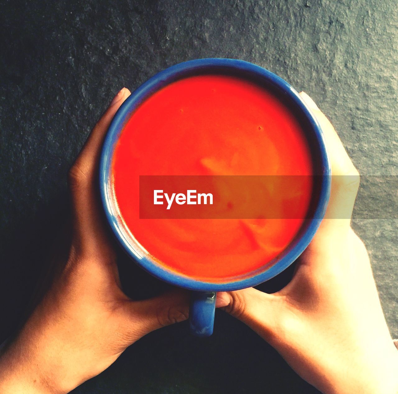 Close-up of hand holding cup of soup on table