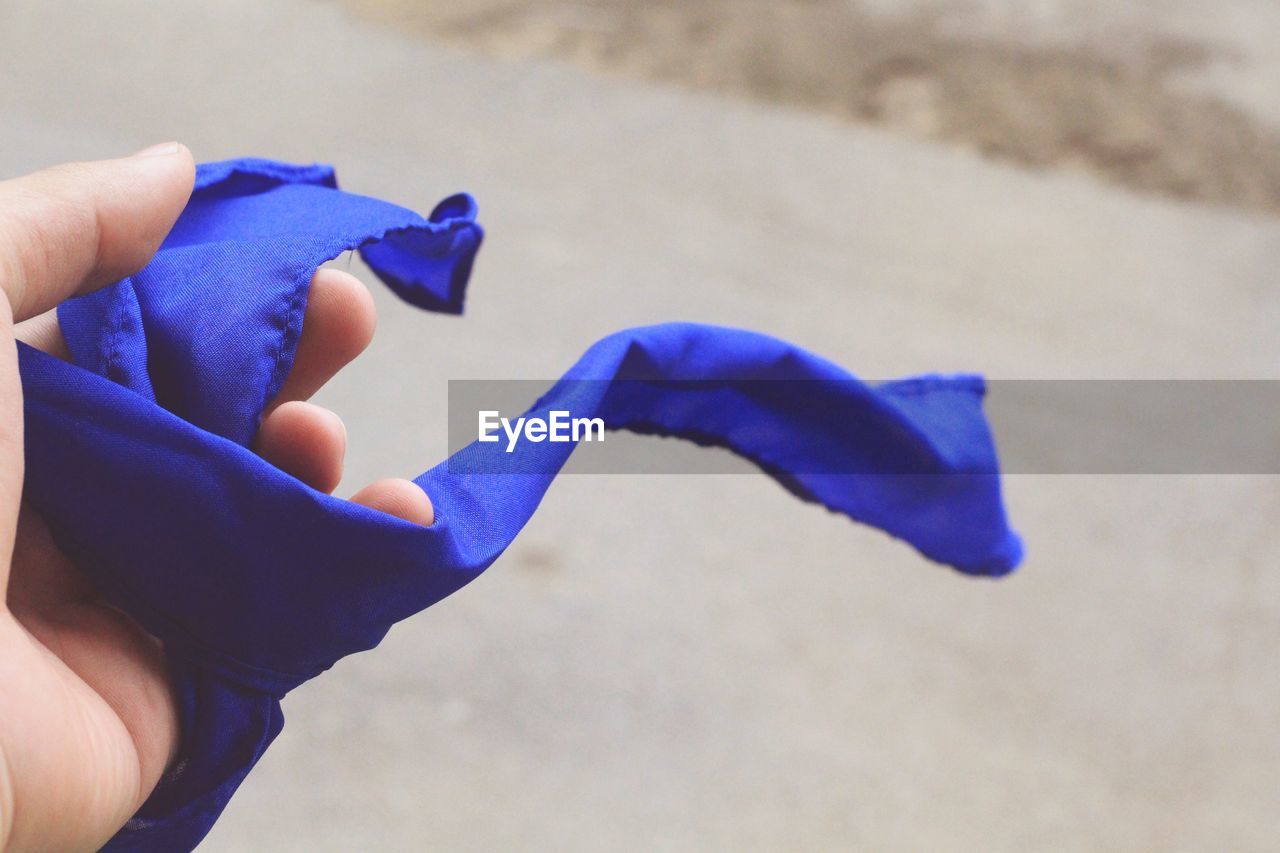 Cropped hand of person holding blue textile on road