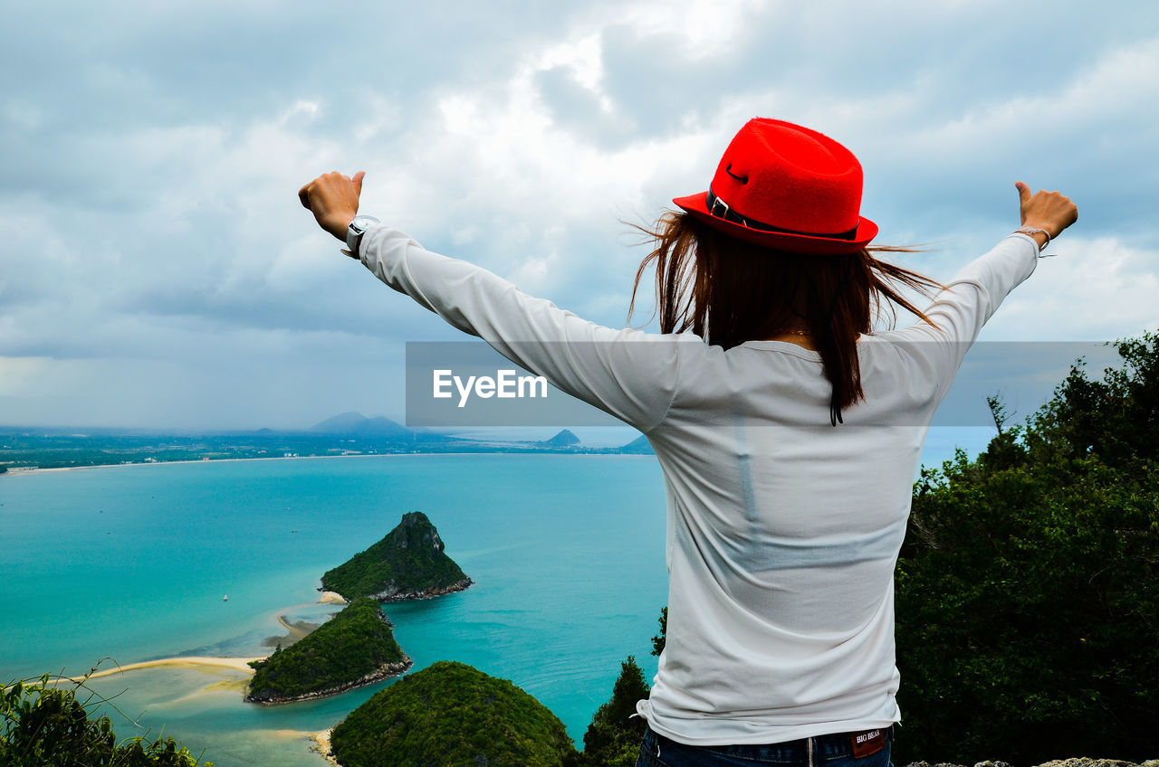 Rear view of woman with arms outstretched standing by sea against sky