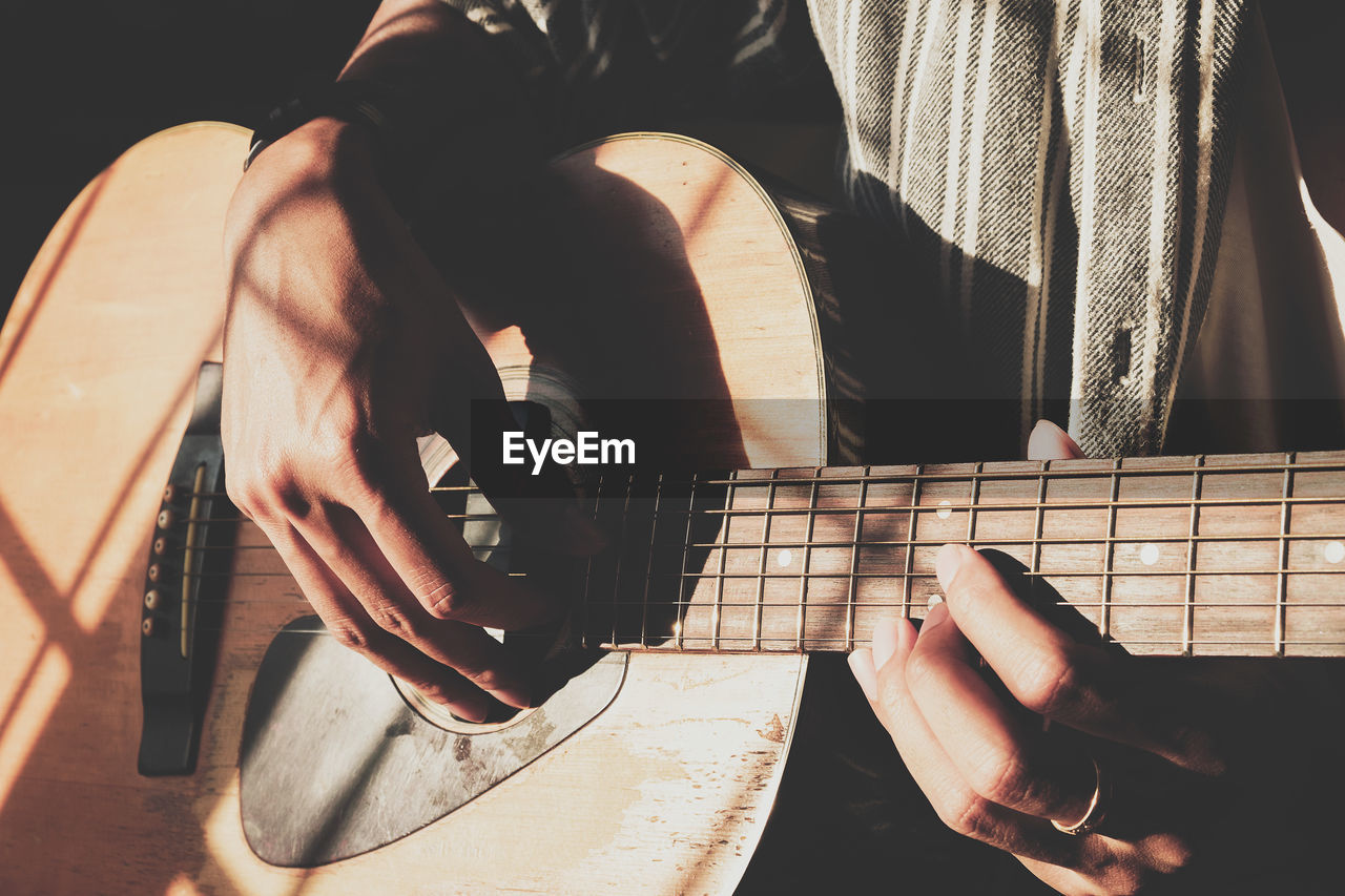 Midsection of man playing acoustic guitar