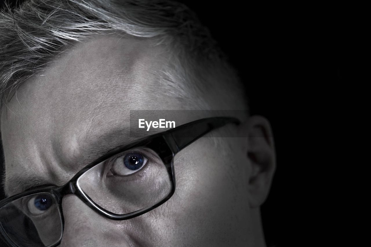 Cropped portrait of man wearing eyeglasses against black background