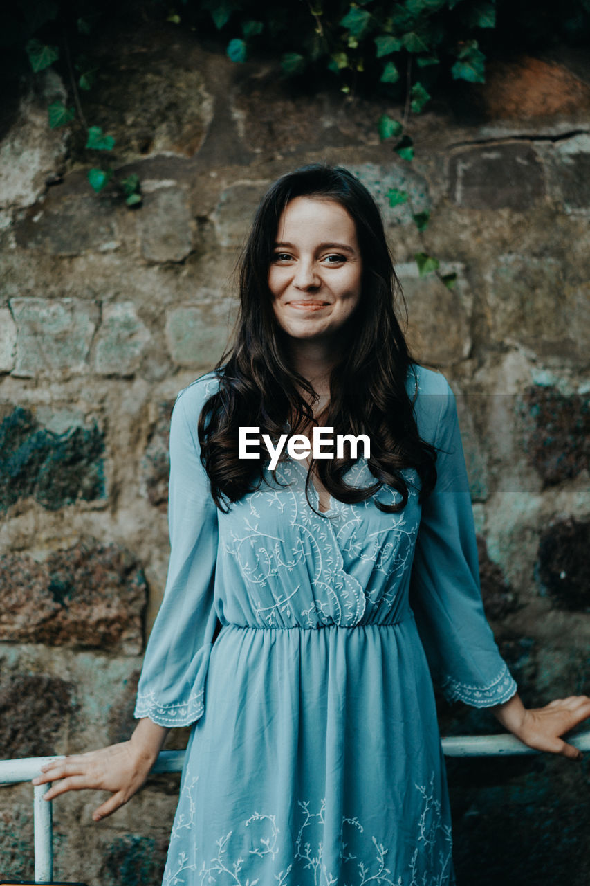 PORTRAIT OF A SMILING WOMAN STANDING AGAINST WALL