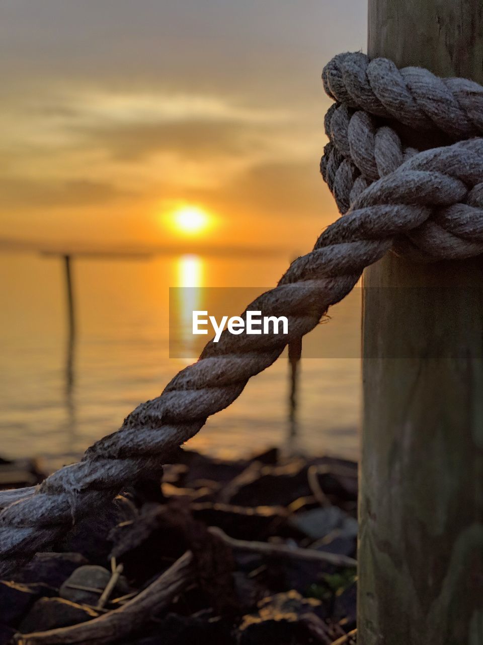 Close-up of rope tied on wooden post during sunrise