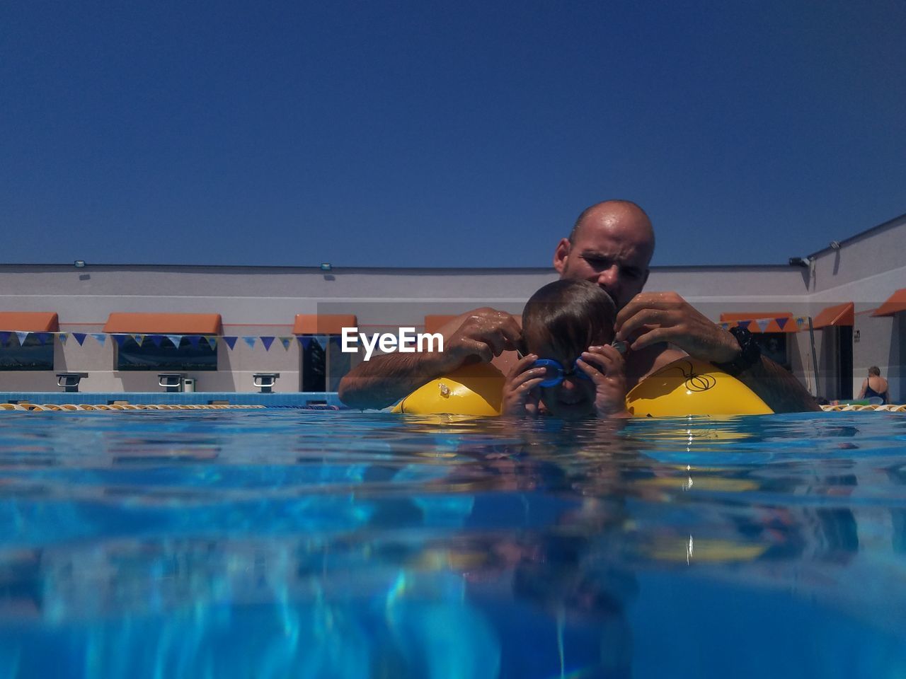 Father and son swimming in pool against clear blue sky