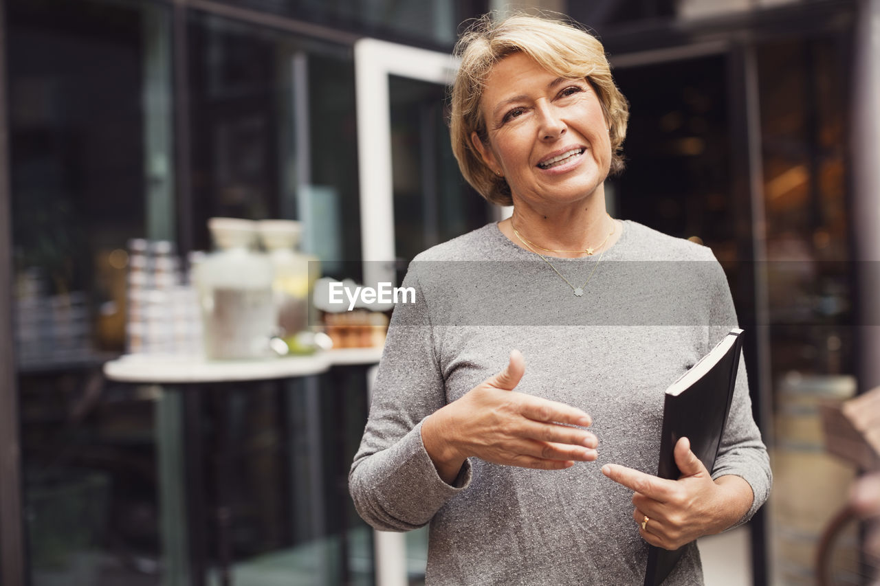 Happy businesswoman gesturing while standing at sidewalk cafe