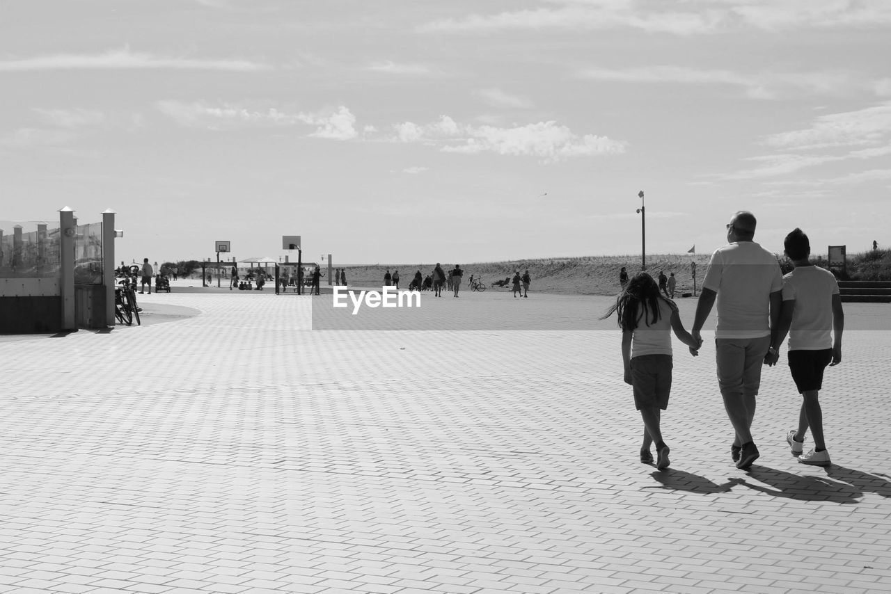 REAR VIEW OF PEOPLE WALKING ON SHORE