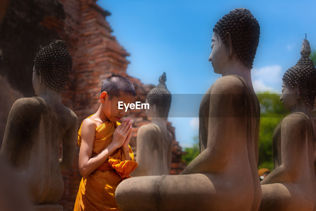 Boy praying while standing by buddha statue