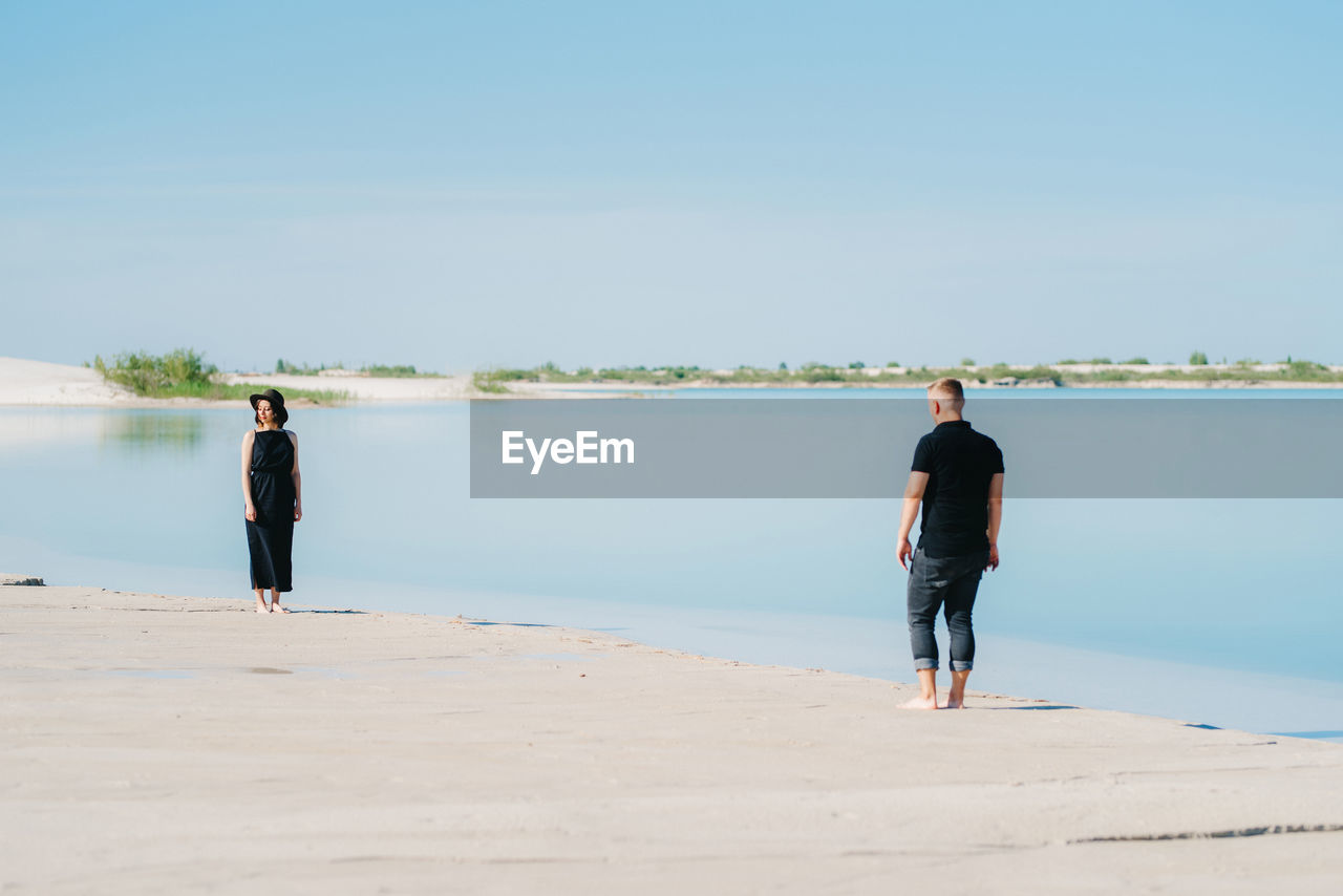 REAR VIEW OF MAN STANDING ON BEACH