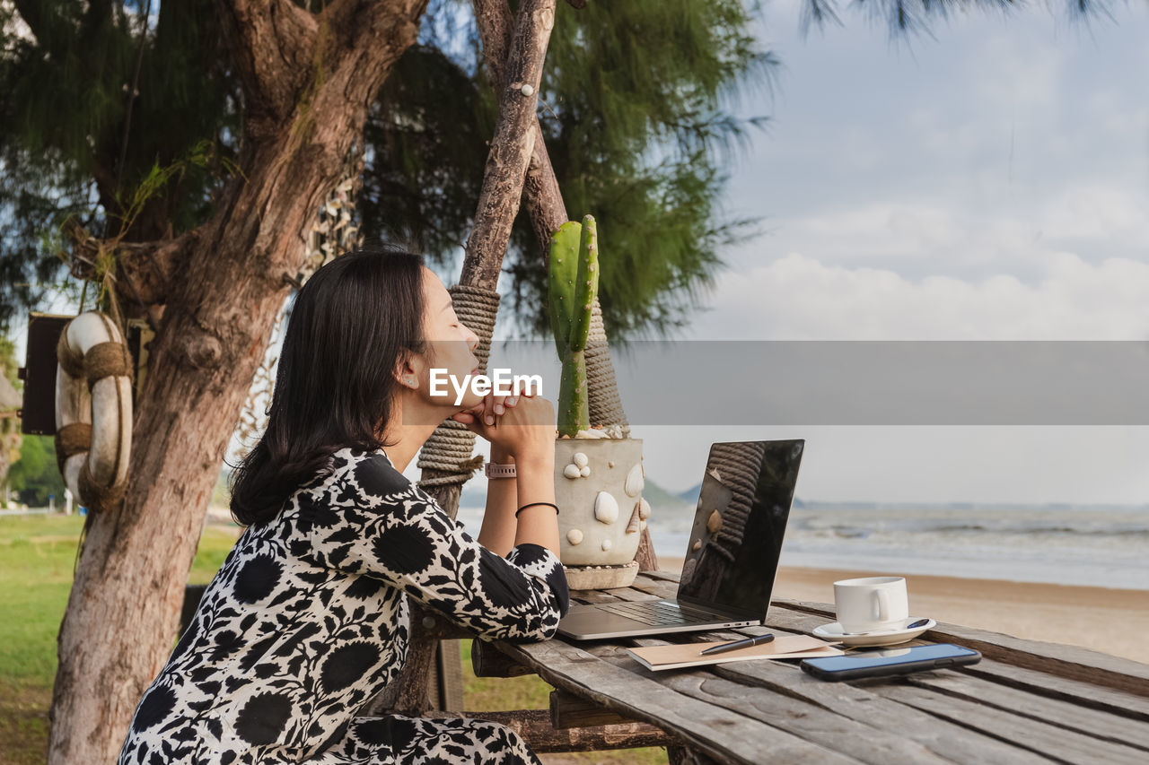 Business woman relaxing breathing fresh air while working with computer on the beach.