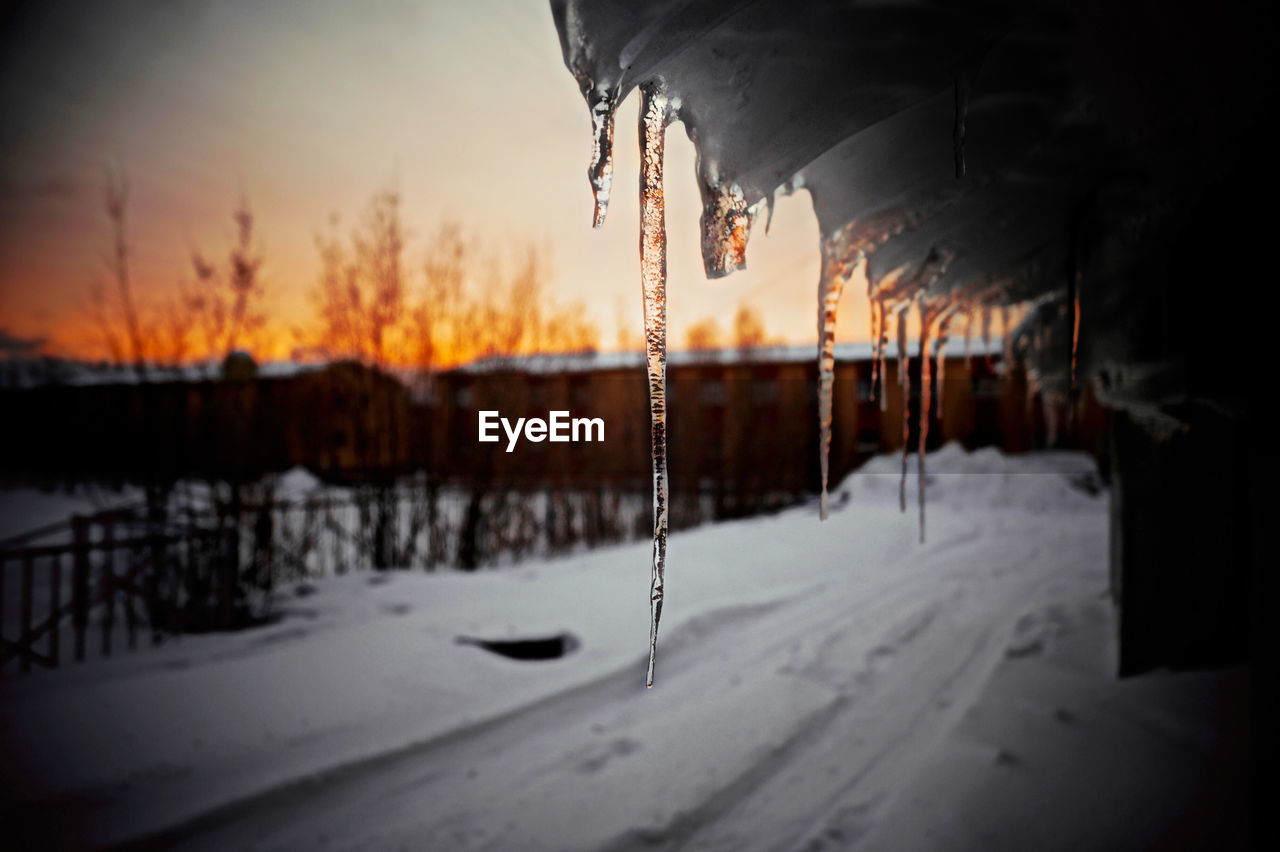 Icicles hanging from roof by snowcapped road during sunset