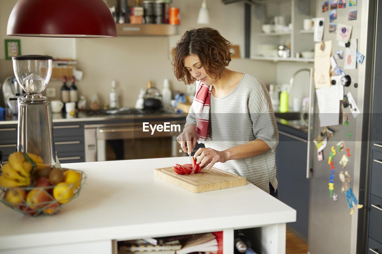 Mature woman cutting tomato in kitchen