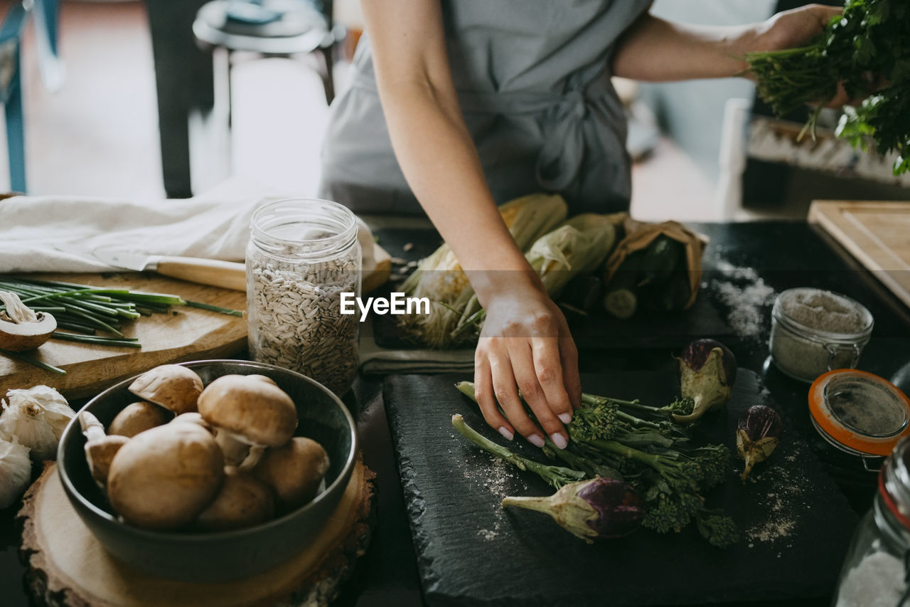 Female chef arranging broccolini and aubergines on slate at counter in studio kitchen